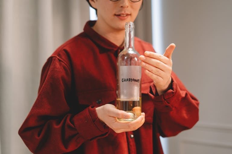 Close-up of a person in red holding a Chardonnay wine bottle indoors, highlighting wine culture.