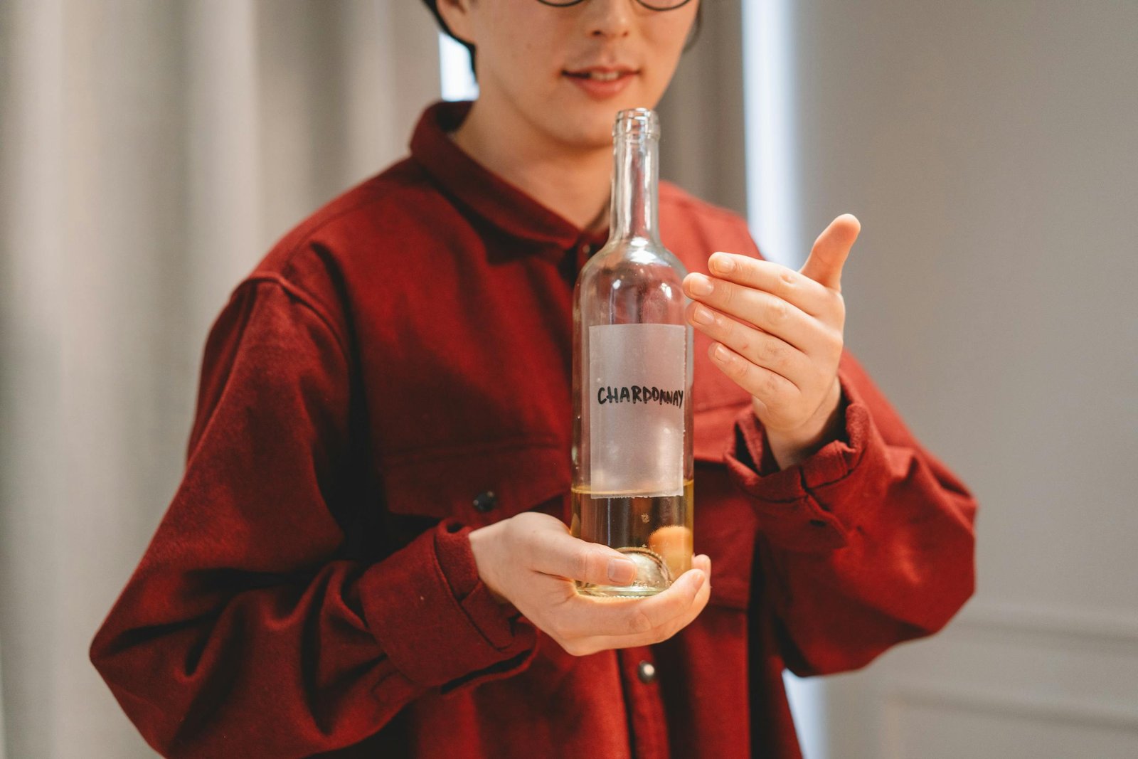 Close-up of a person in red holding a Chardonnay wine bottle indoors, highlighting wine culture.
